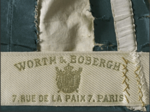 Etiquette apposée sur les créations de la maison Worth et sur laquelle figure l'adresse de la mythique institution domiciliée au 7 rue de la Paix à Paris, Robe de jour, Maison Worth & Bobergh, palaisgalliera.paris.fr