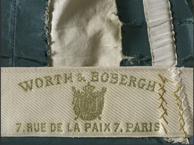 Etiquette apposée sur les créations de la maison Worth et sur laquelle figure l'adresse de la mythique institution domiciliée au 7 rue de la Paix à Paris, Robe de jour, Maison Worth & Bobergh, palaisgalliera.paris.fr